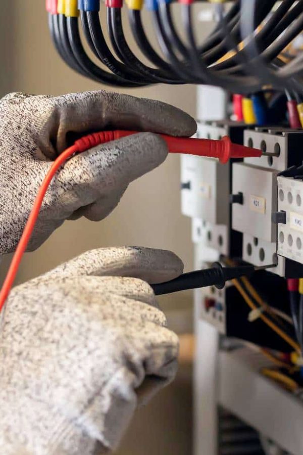 Electrician engineer uses a multimeter to test the electrical installation and power line current in an electrical system control cabinet.