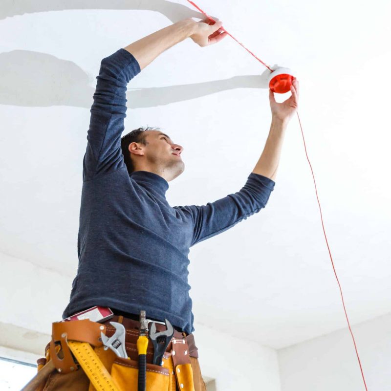 Electrician installing fire alarm system indoors