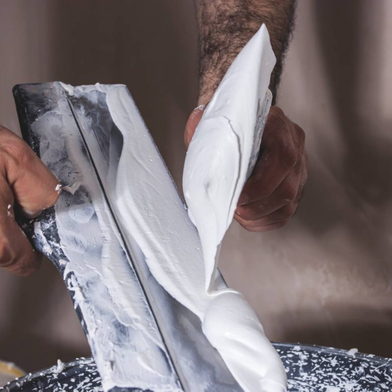 Close-up of a worker putting white putty on a spatula.